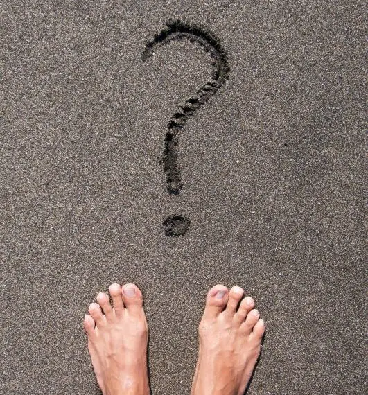 Person standing on black sand beach in front of question mark